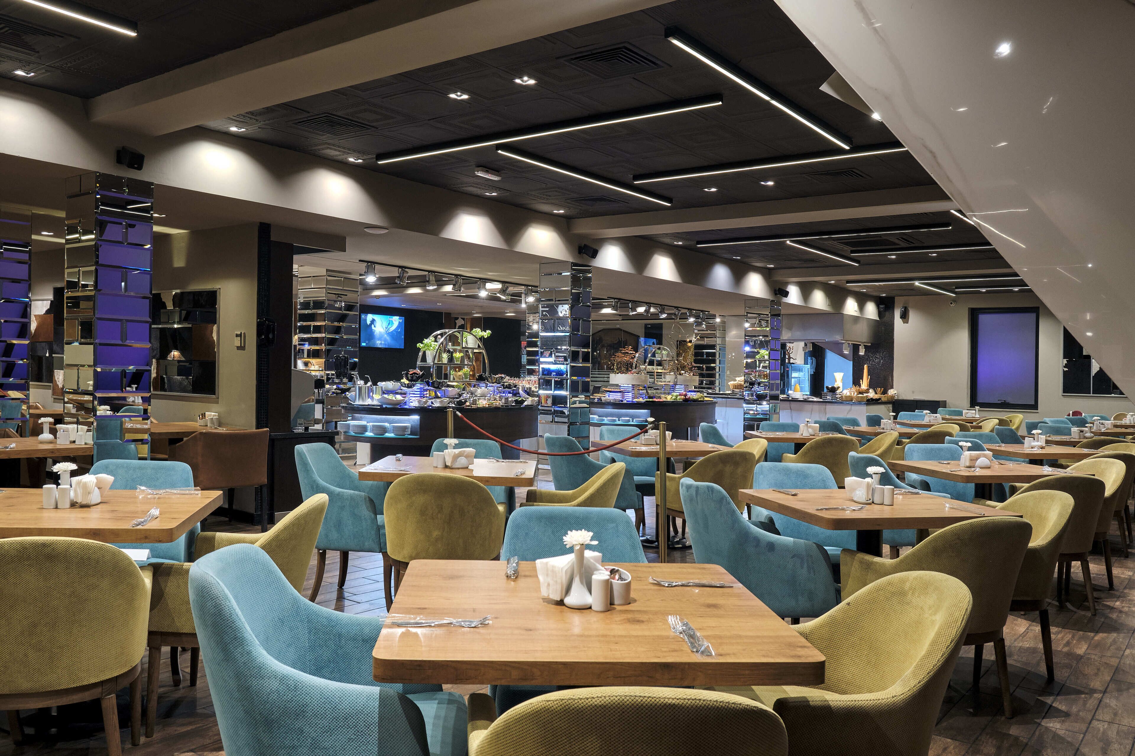 A modern restaurant with multiple tables and chairs, a bar area, and a television screen.