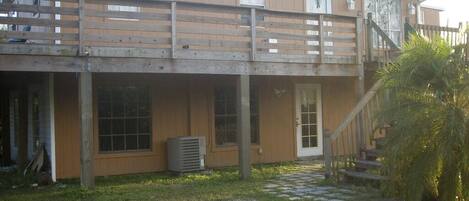 A two-story building with a wooden deck, a front door, and a staircase leading to the upper level.