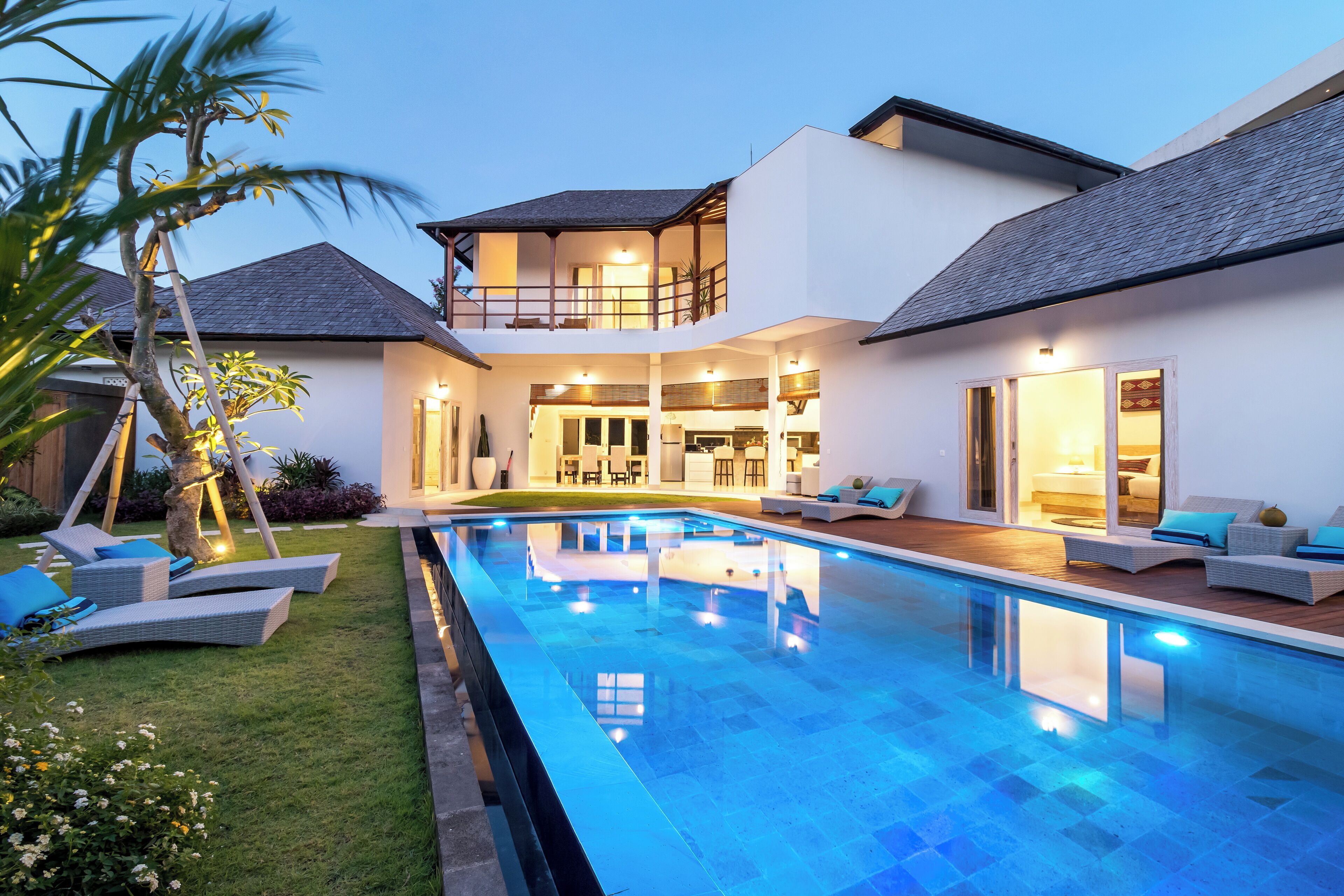 A two-story house with a swimming pool, outdoor seating, and a well-lit interior.