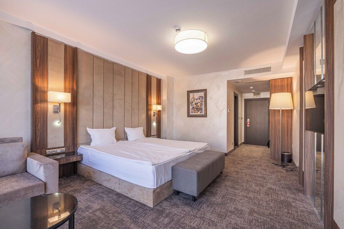 A hotel room with a large bed, a sofa, a small table, and a bench.