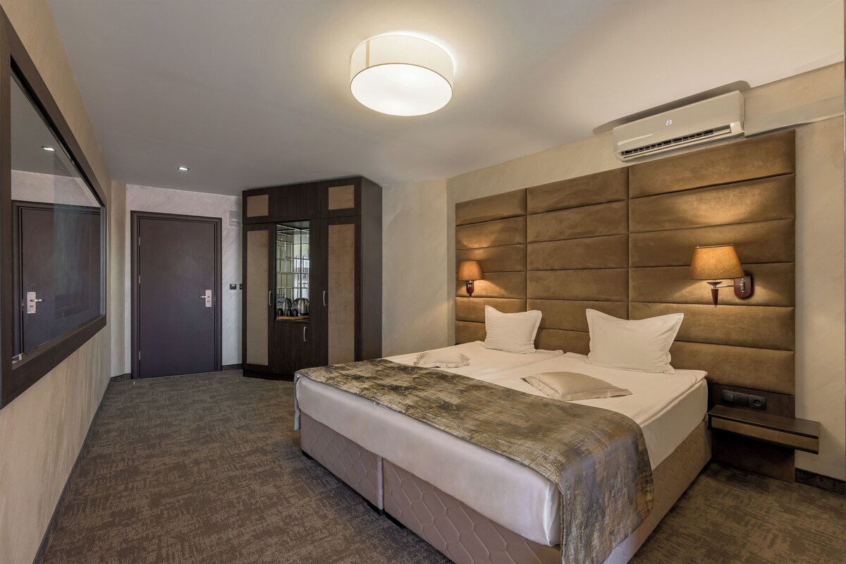 A hotel room with a large bed, bedside lamps, an air conditioning unit, and a view of the hallway.