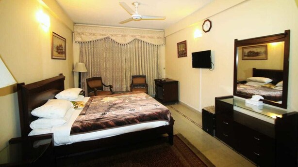 A hotel room with a bed, a ceiling fan, a TV, a mirror, and a clock on the wall. - Swat continental hotel (Swat)