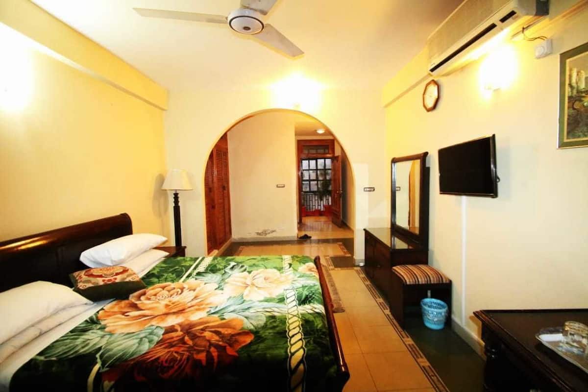 A hotel room with a bed, a desk, a chair, a TV, a clock, and a window.