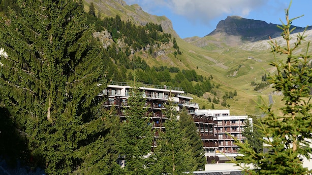 A multi-story hotel with balconies, surrounded by dense green trees and mountains in the background. - Résidence Odalys Le Panoramic (Araches-la-Frasse)