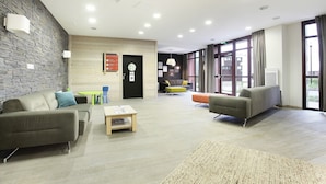 A modern hotel lobby with a stone wall, a wooden door, and a seating area with sofas and a coffee table. - Résidence Odalys Le Panoramic (Araches-la-Frasse)