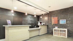 A reception area with a wooden reception desk, a black wall with a stone pattern, and a small shelf with brochures. - Résidence Odalys Le Panoramic (Araches-la-Frasse)
