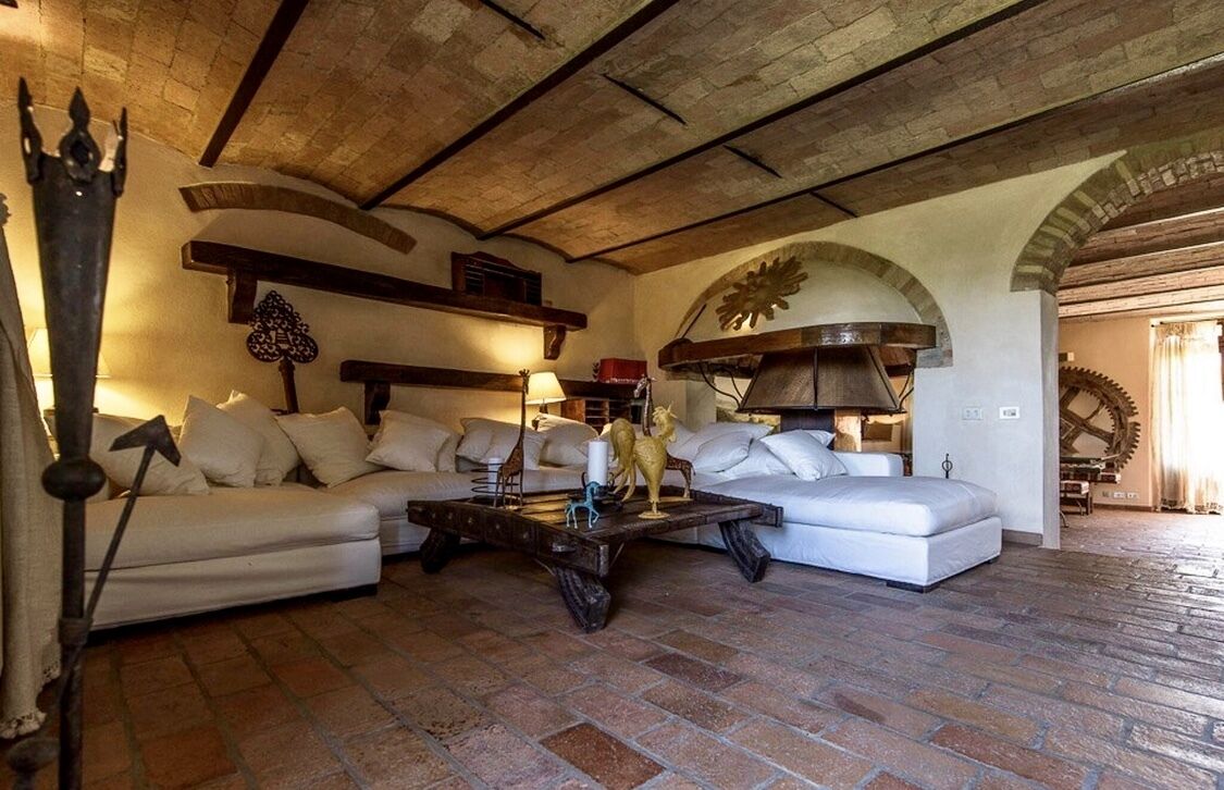 A rustic living room with a stone floor, white sofas, a wooden coffee table, and a large mechanical gear wall piece.