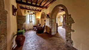Un interior rústico con paredes de ladrillo visto, vigas de madera y suelo de ladrillo. Hay sillones de cuero y una gran planta en maceta.