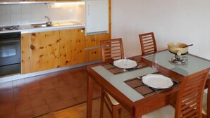 A compact kitchen with wooden cabinets, a built-in oven, and a dining area with a glass table and wooden chairs. - Chaedoz 13 by Interhome (Nendaz)