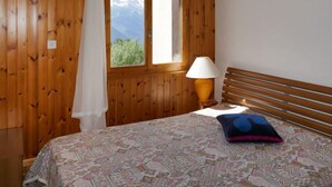 A wooden-paneled room with a bed, a window with a view of mountains, a lamp, and a wall-mounted picture of dogs. - Chaedoz 13 by Interhome (Nendaz)