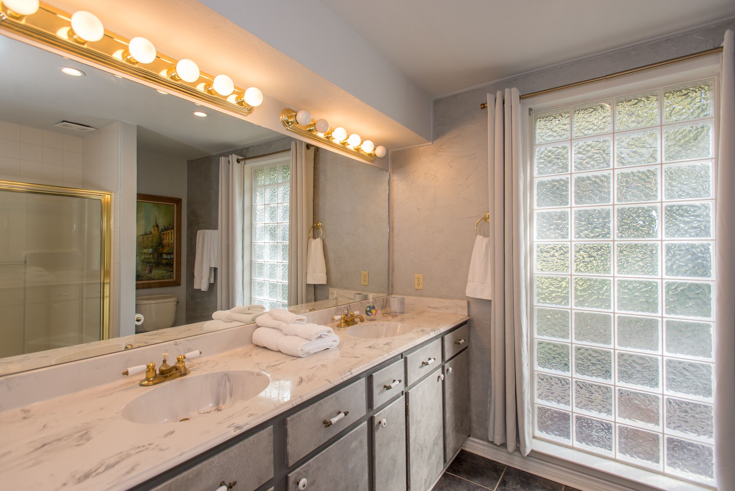 Une salle de bain avec deux lavabos, un grand miroir et une fenêtre en verre dépoli.