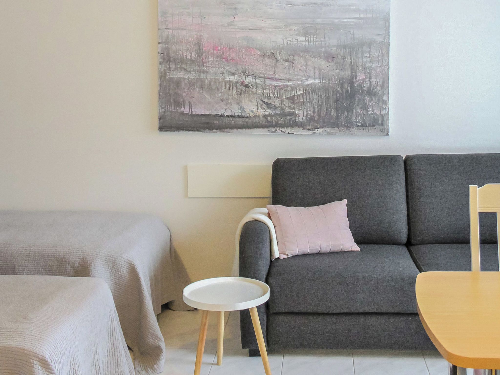 A modern living room with a grey sofa, a small round table, and a bed with a grey cover.