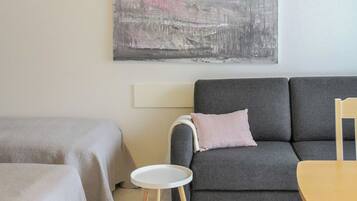 A modern living room with a grey sofa, a small round table, and a bed with a grey cover.