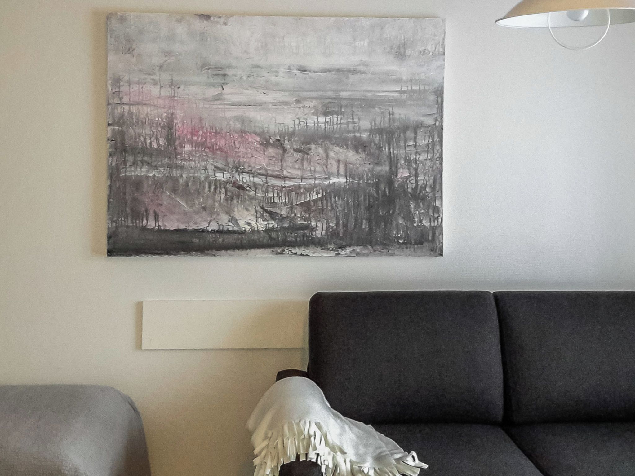 Ein modernes Wohnzimmer mit einem grauen Sofa, einem weißen Zierkissen und einem großen abstrakten Gemälde an der Wand.