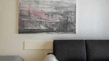 Ein modernes Wohnzimmer mit einem grauen Sofa, einem weißen Zierkissen und einem großen abstrakten Gemälde an der Wand.