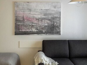 Una sala de estar moderna con un sofá gris, un cojín decorativo blanco y un cuadro abstracto grande en la pared.