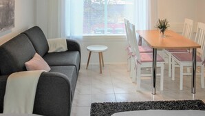 Moderni olohuone, jossa on harmaa sohva, pieni pyöreä pöytä ja ruokailutila, jossa on valkoiset tuolit ja puinen pöytä.