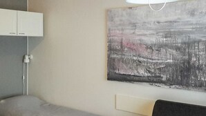 Moderni hotellihuone, jossa on sänky, yöpöytä, lamppu ja taulu seinällä.