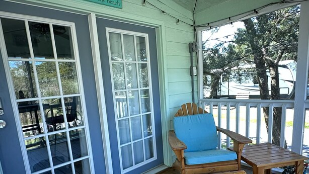 A porch with a wooden chair and table, a door with glass panels, and a sign reading 'The Beach'. - A Gnome Home: Convenient to Restaurants and Coffee Shops (Ocracoke)
