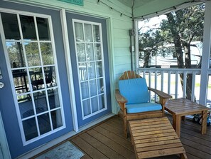 A porch with a wooden chair and table, a door with glass panels, and a sign reading 'The Beach'.