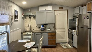 A compact kitchen with a dining table, chairs, a refrigerator, and a microwave. - A Gnome Home: Convenient to Restaurants and Coffee Shops (Ocracoke)