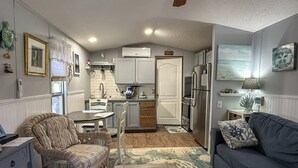A compact living space with a kitchenette, a dining area, and a seating area with a sofa and a wicker chair. - A Gnome Home: Convenient to Restaurants and Coffee Shops (Ocracoke)