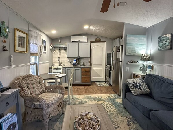 A compact living space with a kitchenette, a dining area, and a seating area with a sofa and a wicker chair.