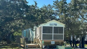 A mobile home with a screened porch, a small deck, and a gravel driveway. - A Gnome Home: Convenient to Restaurants and Coffee Shops (Ocracoke)
