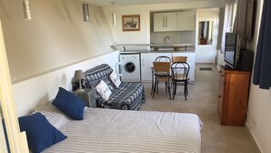 A compact bedroom with a bed, two chairs, a washing machine, and a small kitchenette. - Three star studio (Sète)