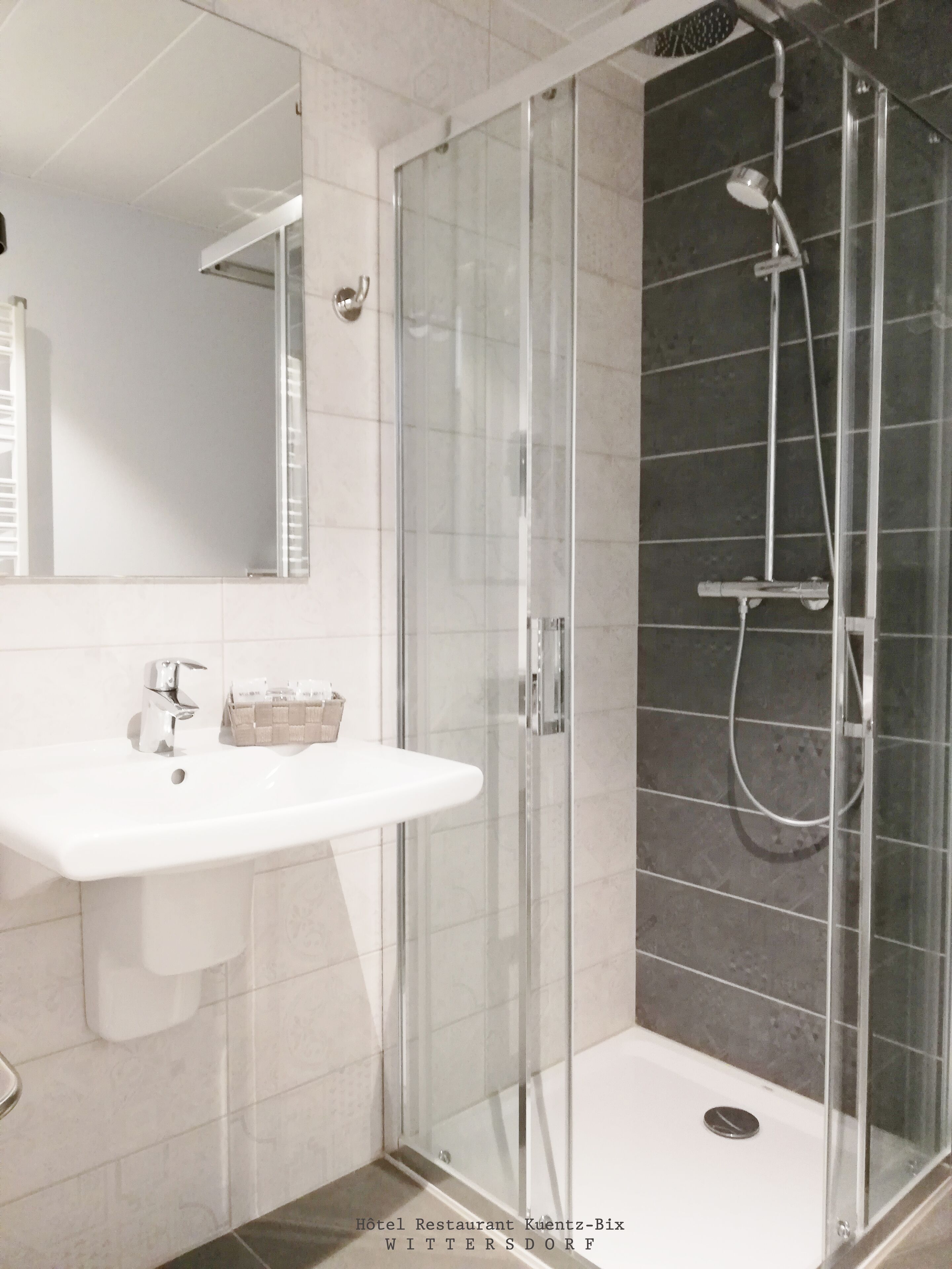 Une salle de bain moderne avec une douche à parois de verre, un lavabo blanc et un miroir.
