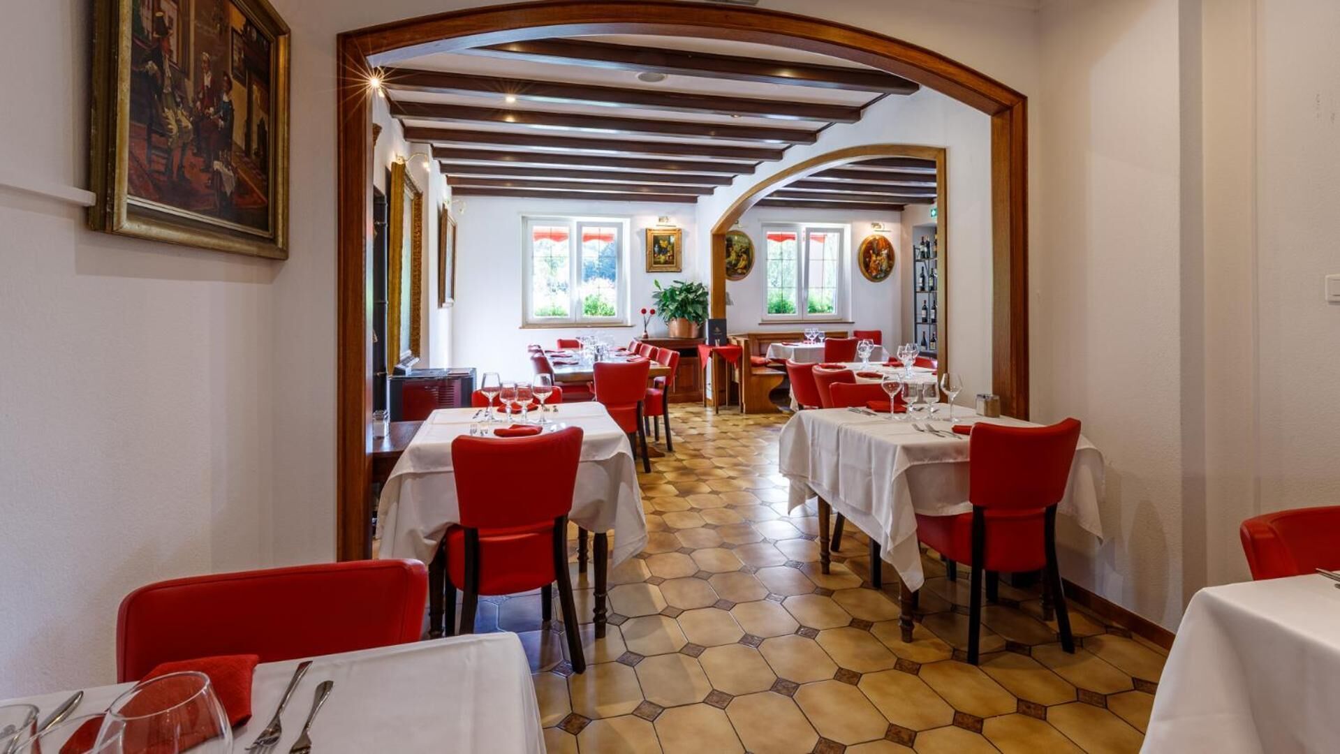 A restaurant with red chairs and white tablecloths, a tiled floor, and a wooden ceiling.