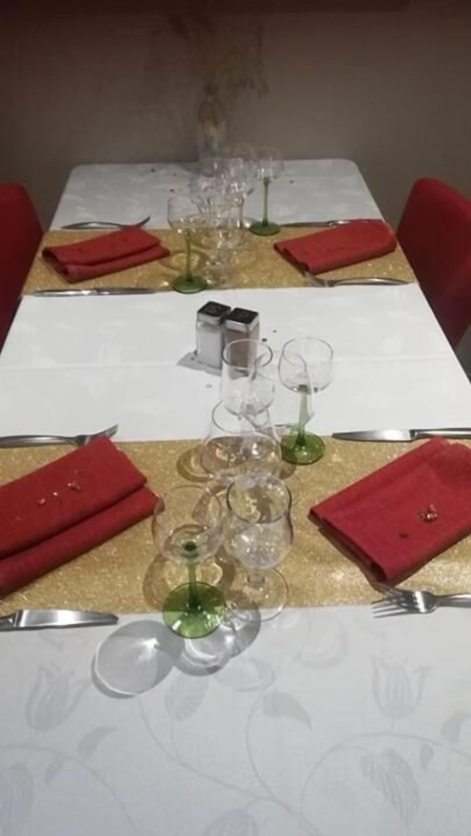 Ein Esstisch ist gedeckt mit roten Servietten, klaren Weinkelchen und Besteck.