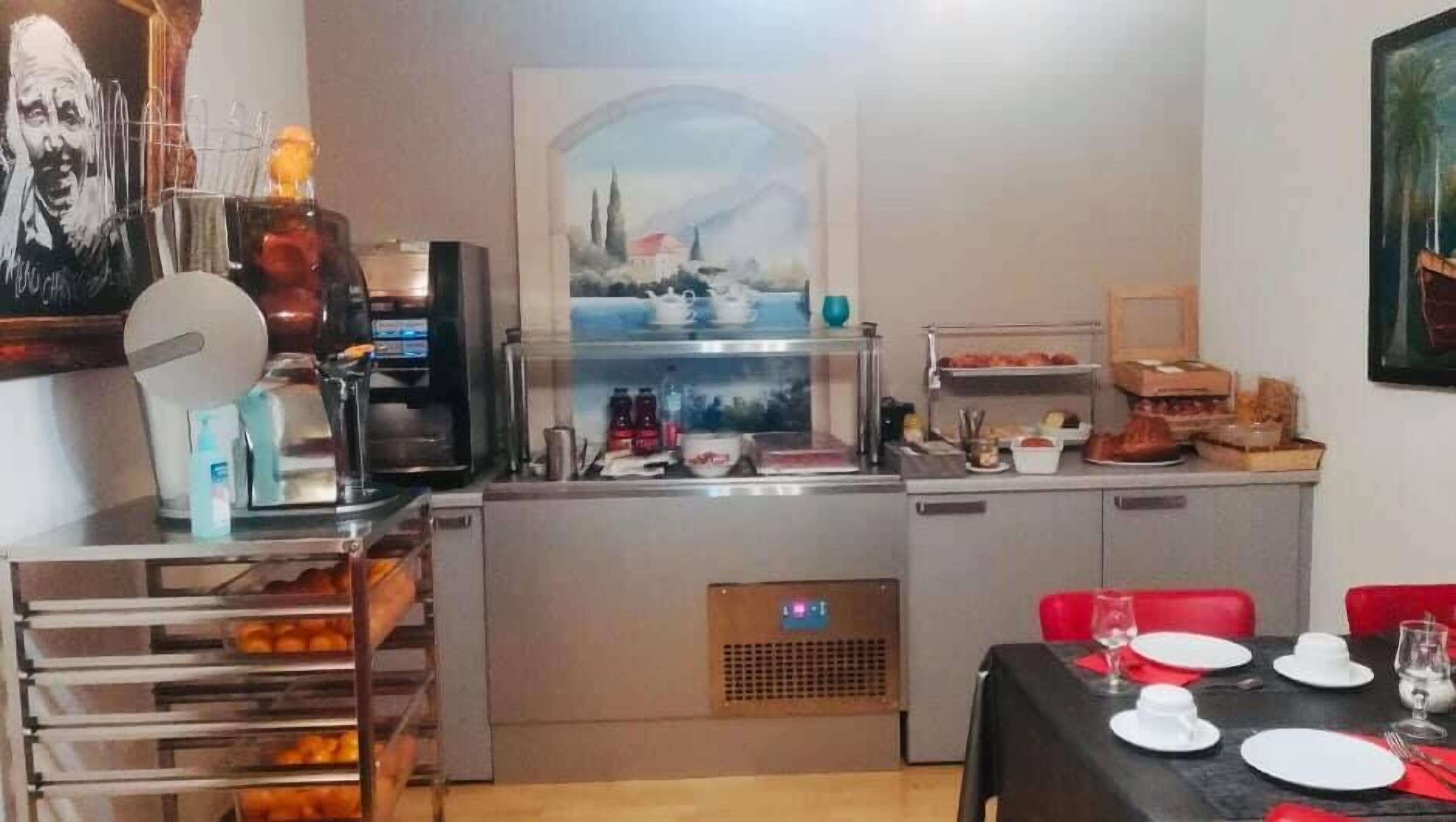 A compact kitchen with a coffee machine, a small refrigerator, and a microwave. There is a dining area with a table set for two, and a window with a view of a building.