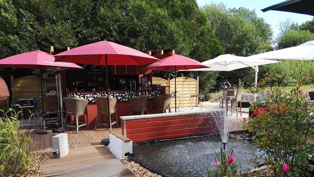A wooden deck with outdoor seating, a small pond, and umbrellas. - Hotel Restaurant Kuentz (Wittersdorf)