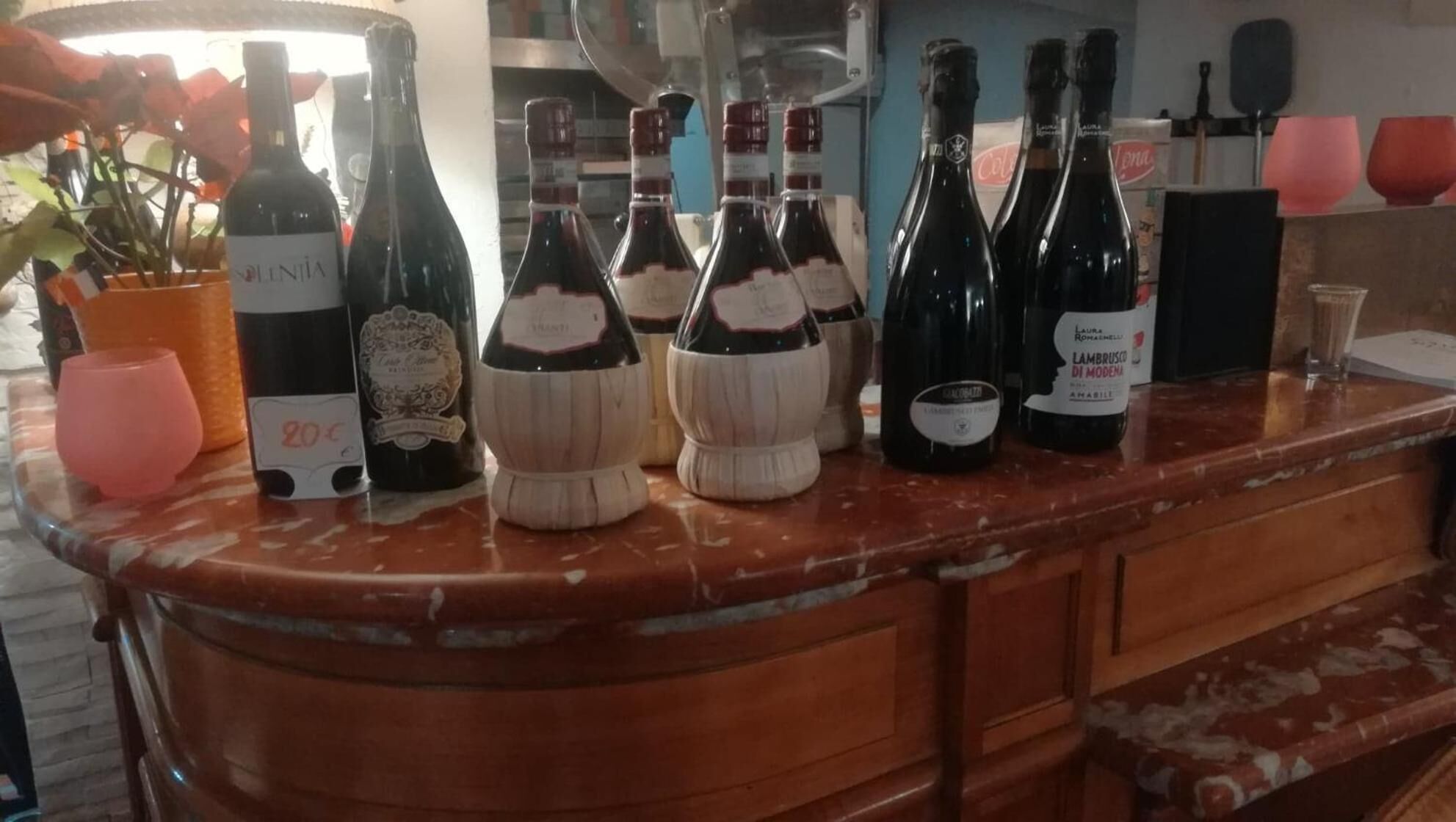 A bar counter with various bottles of wine and a few glasses.