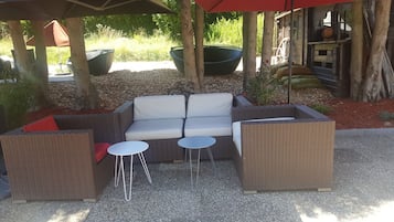 A wicker sofa set with two small tables, surrounded by trees and outdoor furniture.