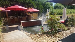 A wooden deck with outdoor seating, a water feature, and red umbrellas. - Hotel Restaurant Kuentz (Wittersdorf)