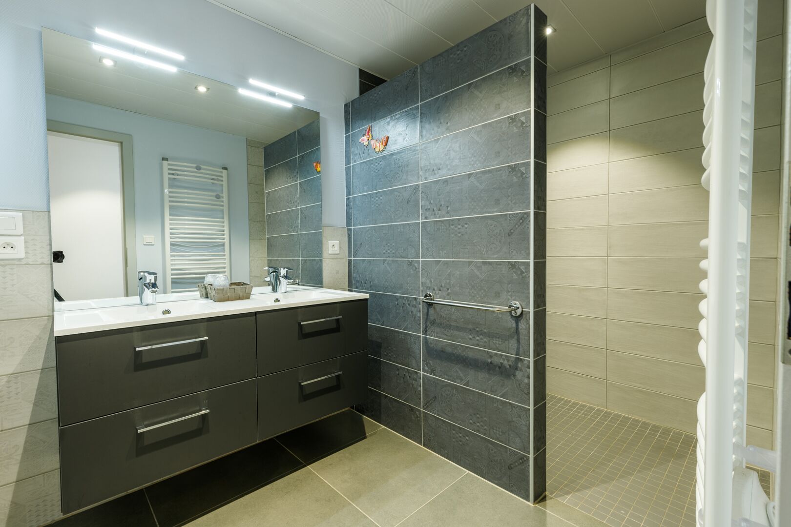 A modern bathroom with a dark tiled wall, a white sink, and a mirror.