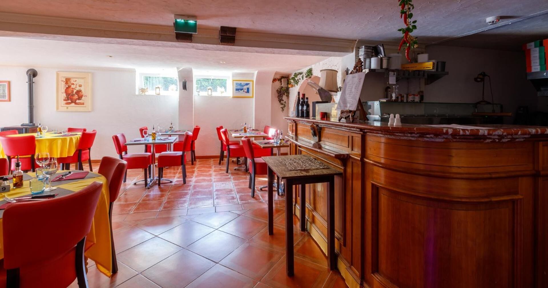 A spacious dining area with red chairs and yellow tablecloths, a wooden bar counter, and tiled flooring.
