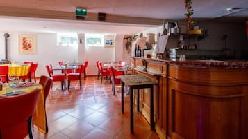 A spacious dining area with red chairs and yellow tablecloths, a wooden bar counter, and tiled flooring.