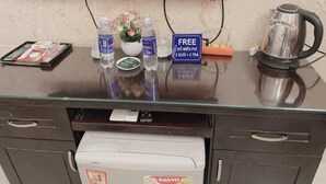 Mostrador de recepción de hotel con televisión de pantalla plana, cafetera, agua embotellada, arreglo floral y un cartel de oferta de regalo gratuito.