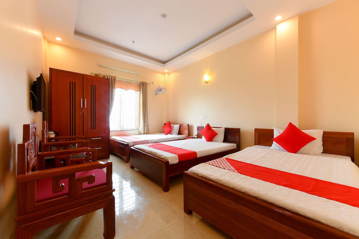 A hotel room with three beds, wooden furniture, and a television.