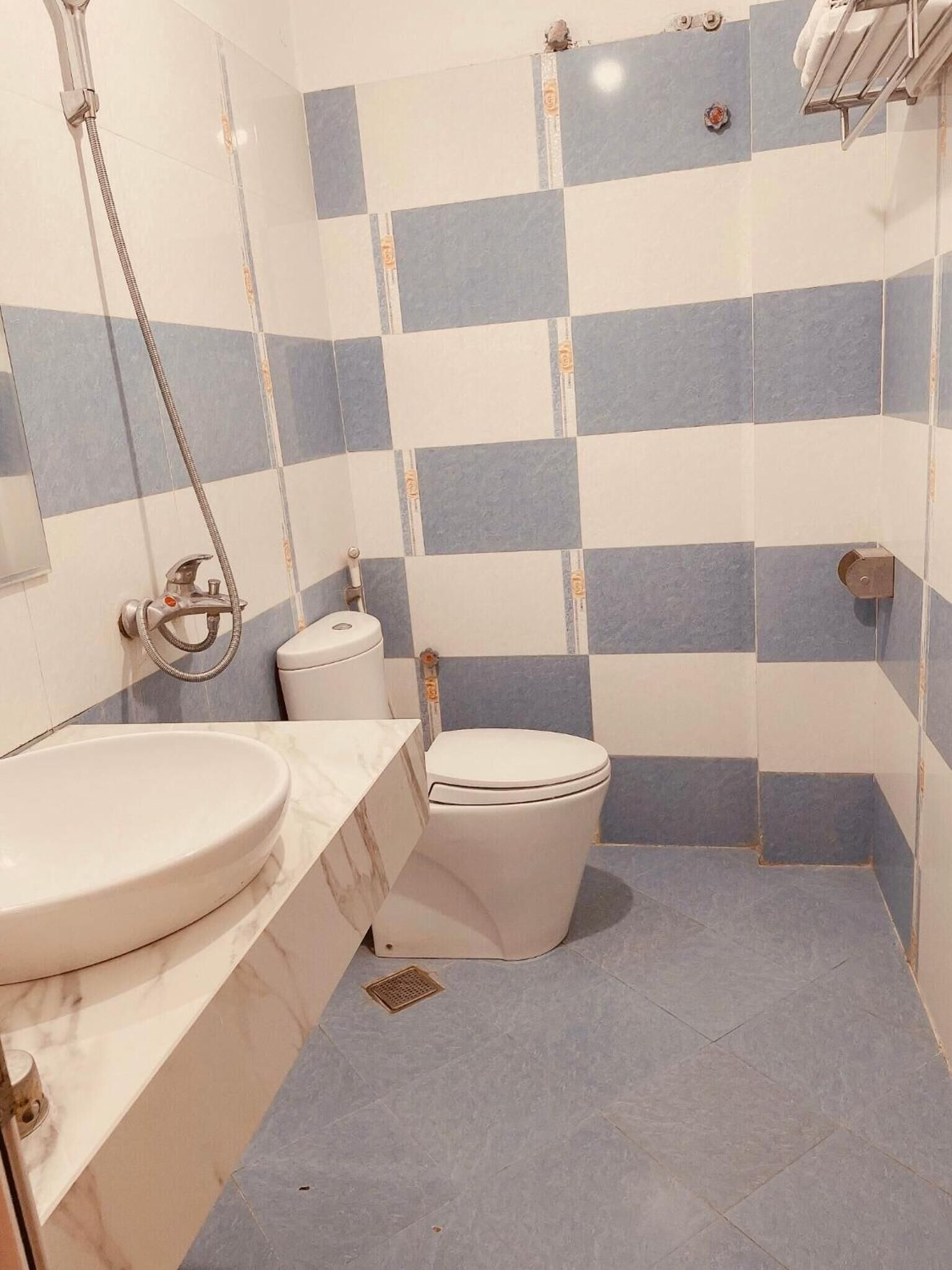 Casa de banho com parede de azulejos xadrez, sanita, lavatório e chuveiro.