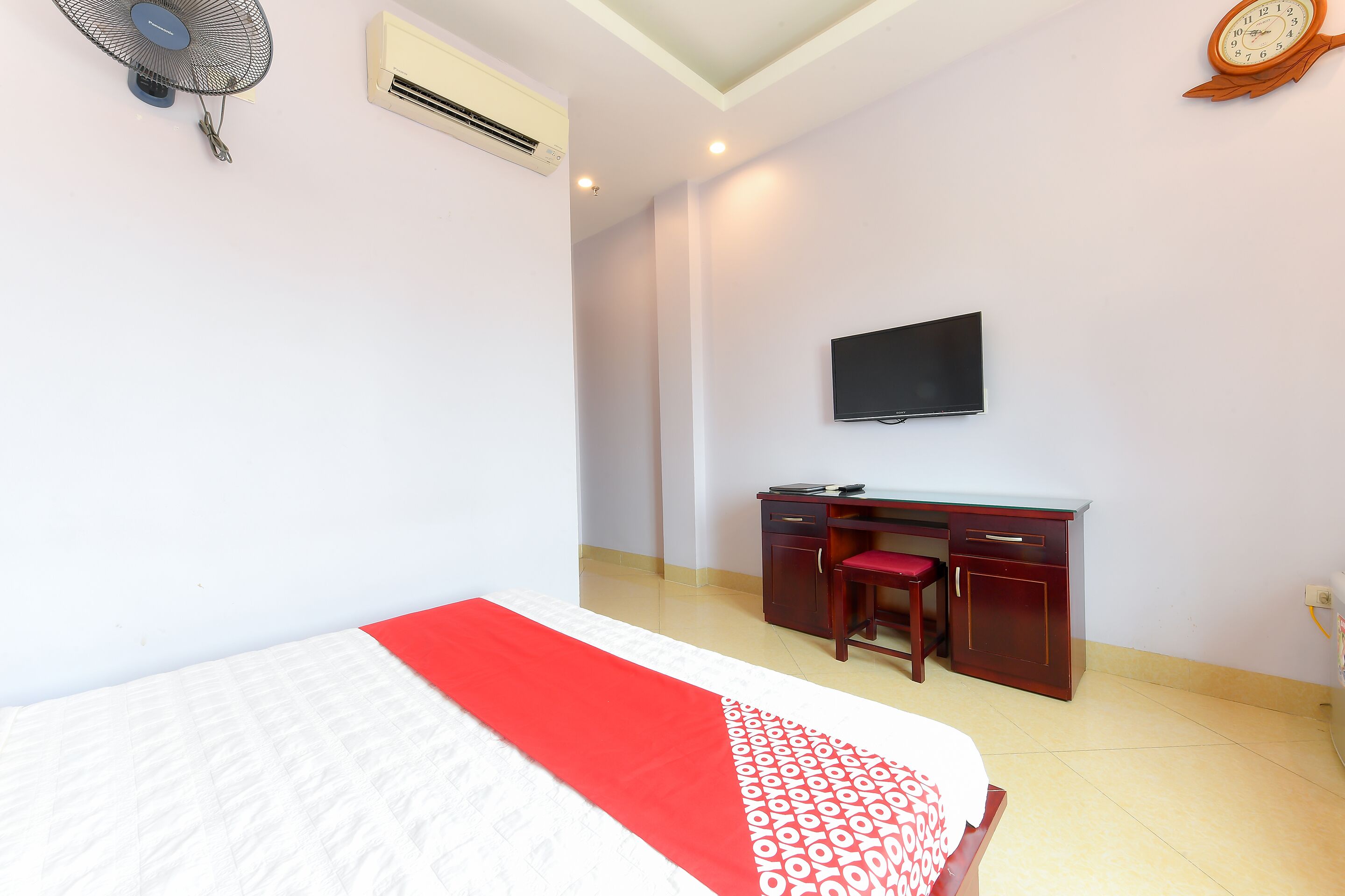 A hotel room with a bed, a desk, a chair, a TV, and an air conditioning unit.