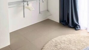 Une pièce avec une étagère métallique adossée au mur, une fenêtre avec des rideaux foncés et un tapis beige sur le sol.