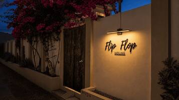 A modern house with a 'Flop House' sign, a wooden door, and a garden with pink flowers.