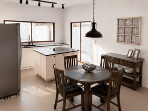 A modern kitchen with a dining area, wooden chairs, a round table, and a hanging light fixture.