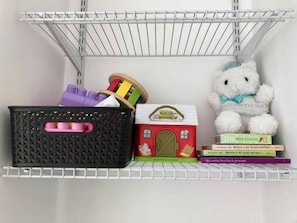 Une étagère avec un panier noir, une petite maison de jeu, un ours en peluche blanc et quelques livres.