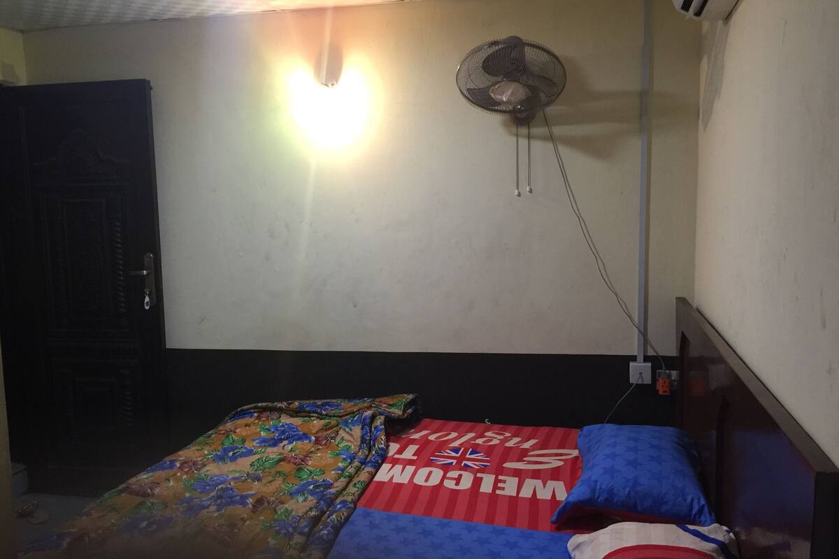 A bedroom with a bed, a wall-mounted fan, and a door.