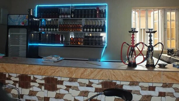 Een bar met een marmeren aanrecht, flessen op planken en waterpijpen.